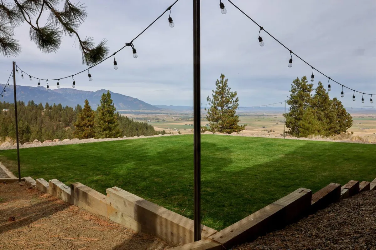 A wide green lawn framed by mountains and illuminated by string lights overhead sets a festive and tranquil tone for evening gatherings, parties, or relaxed outdoor activities. The space suggests both intimacy and the ability to entertain larger groups under the stars.