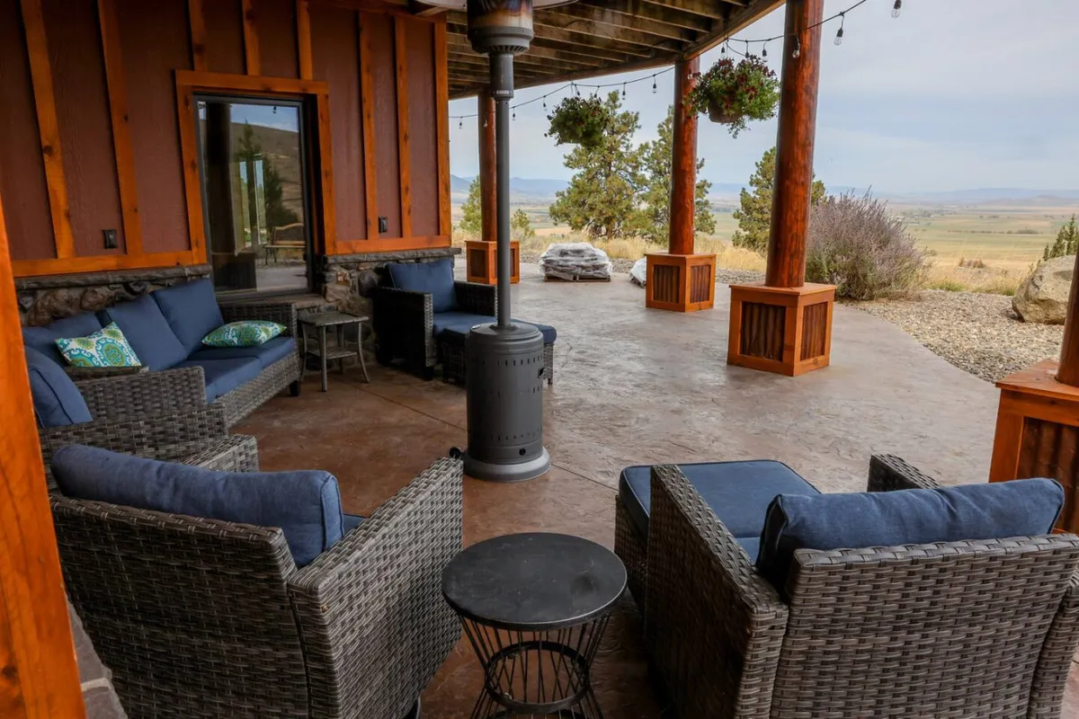 An exterior seating area with wicker furniture arranged around a fire pit, enhanced by hanging plants and sturdy wooden columns. The setting feels intimate yet open to the surrounding nature, inviting guests to gather for warmth and conversation.