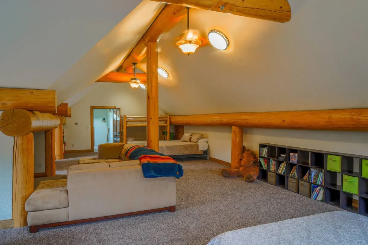 A comfortable, playful bonus room with wooden beams, built-in bunk beds, bookshelves, and sofas. The space is designed for both relaxation and fun, making it inviting for families or groups seeking privacy and enjoyment.