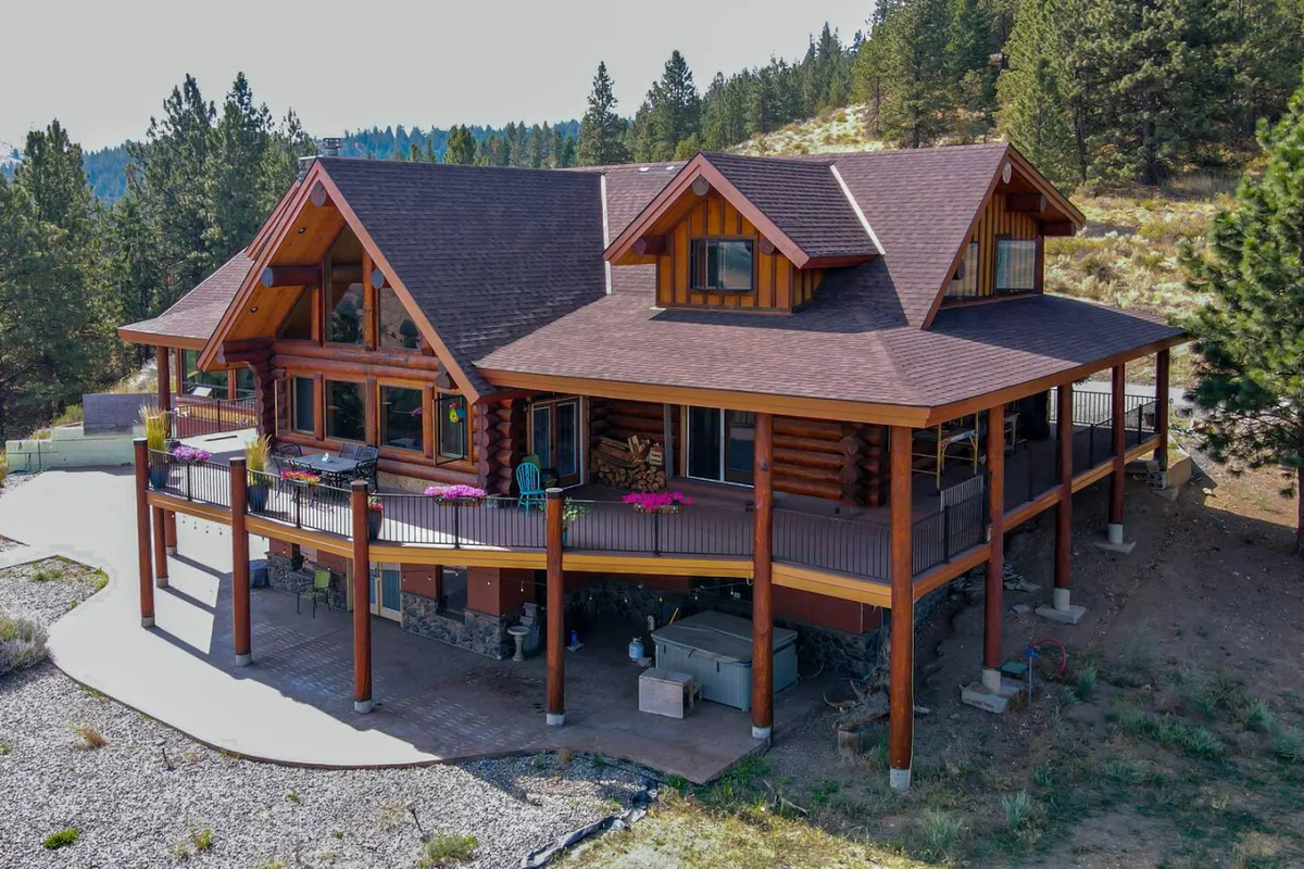 A view of the lodge’s exterior showcasing its log cabin architecture, large windows, an expansive deck area, and a landscaped yard surrounded by trees. The scene suggests ample private parking and easy access to the outdoors.